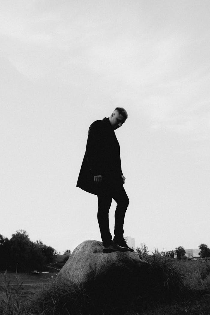 Black and white silhouette of a man standing on a rock outdoors.