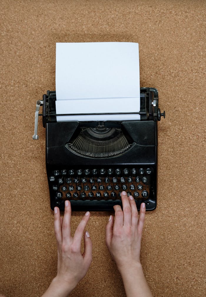Hands typing on a vintage typewriter placed on a corkboard surface, showcasing classic analog technology.
